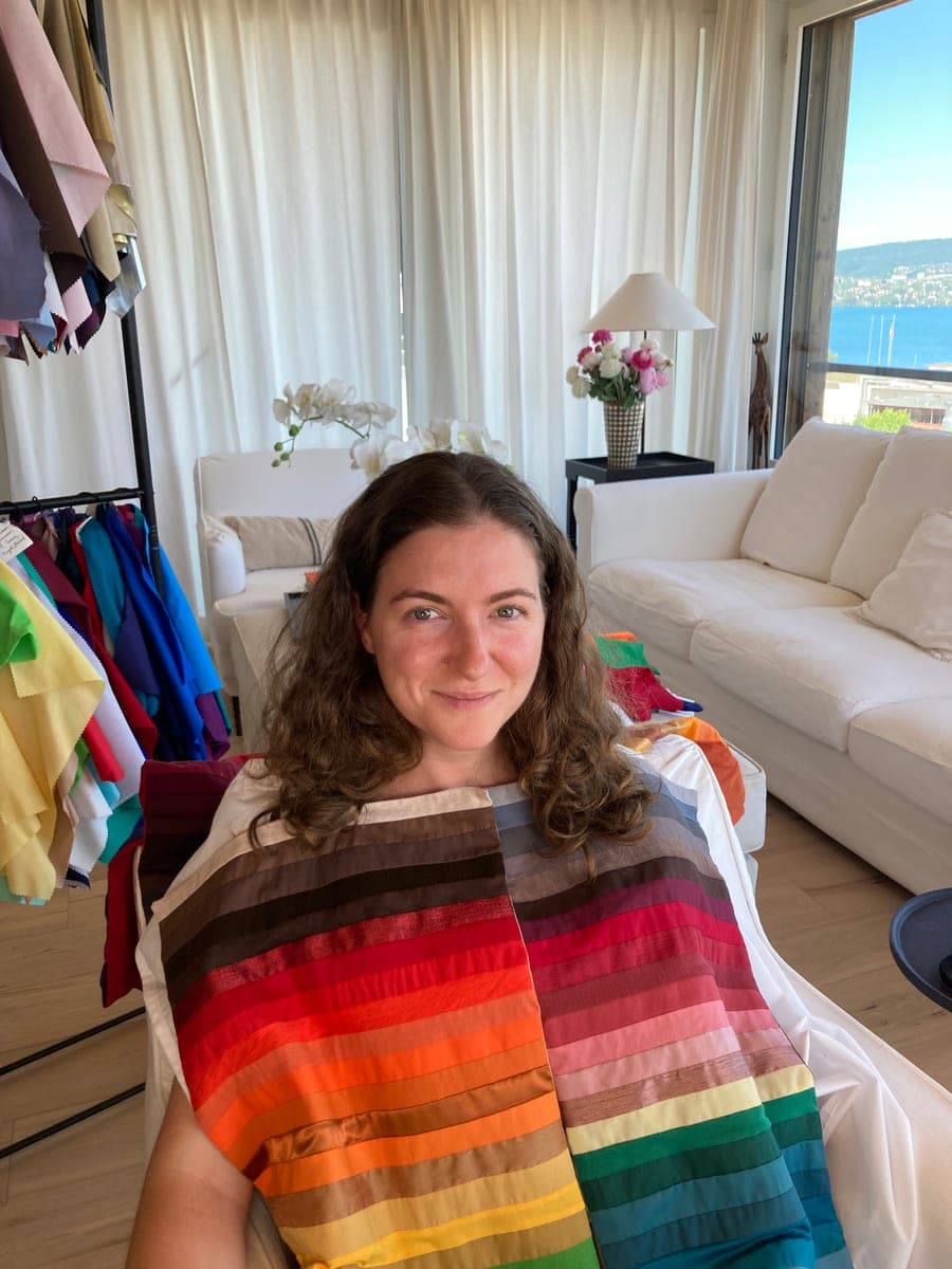 Sabrina seated with a rainbow of seasonal color drapes across her shoulders, color swatches beside her and the Zürich lake behind